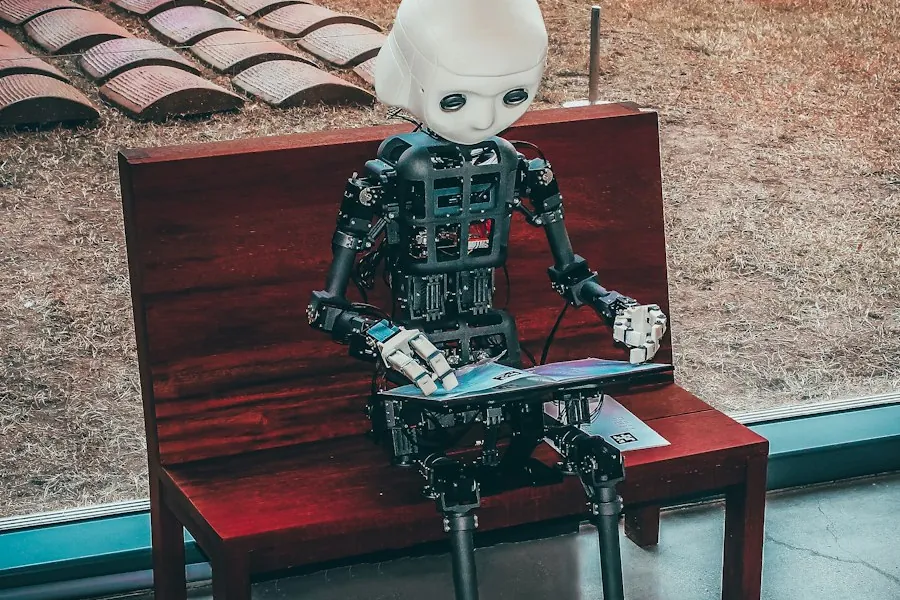 Robot humanoïde assis sur un banc, un écran posé sur les genoux